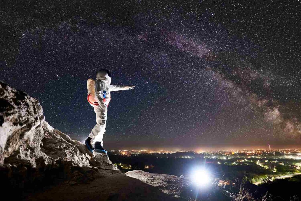 Astronaut standing on rocky mountain under starry night sky, reflecting space exploration themes